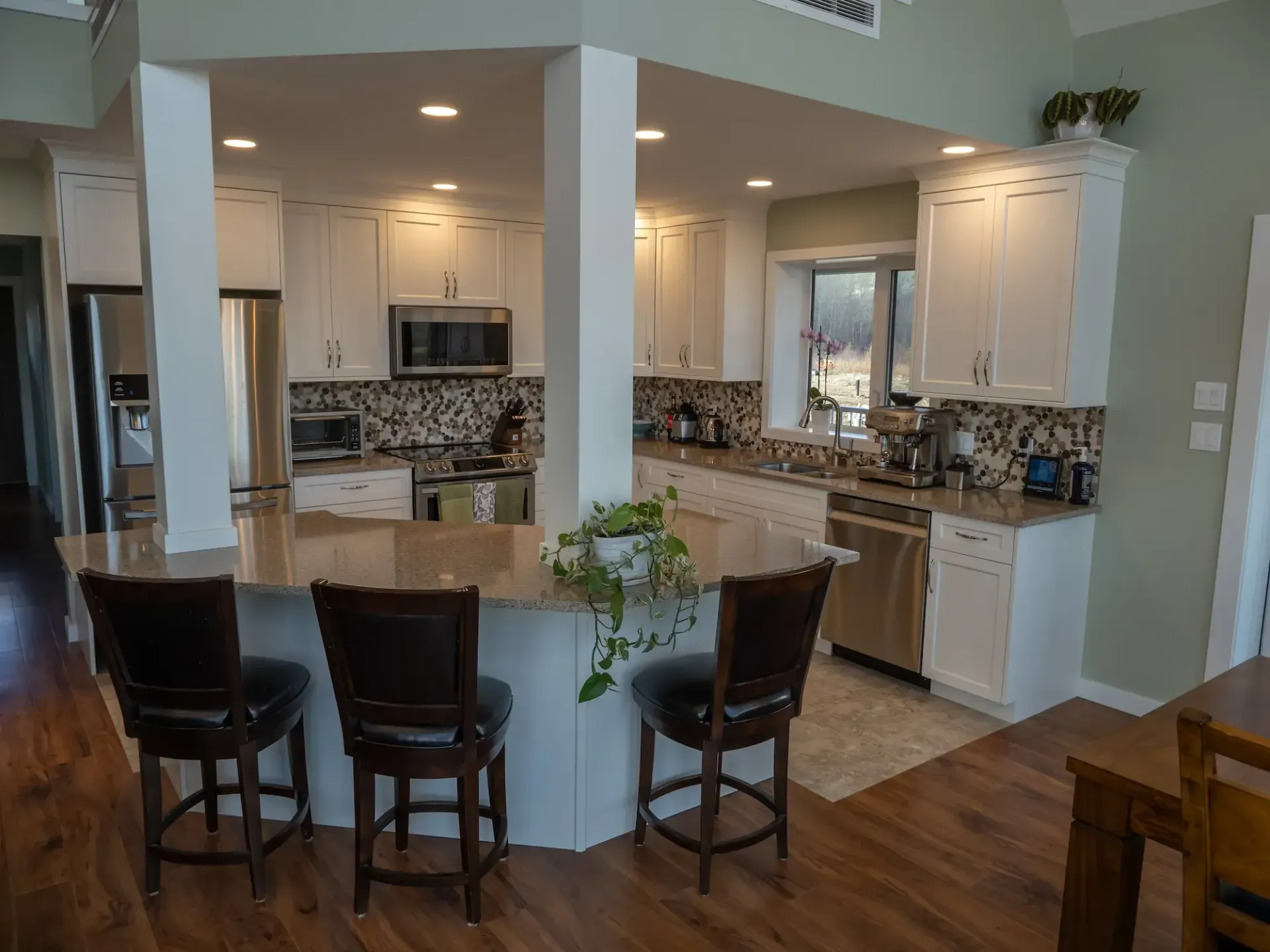Modern kitchen with white cabinets, granite island, and three dark bar stools in an open living space