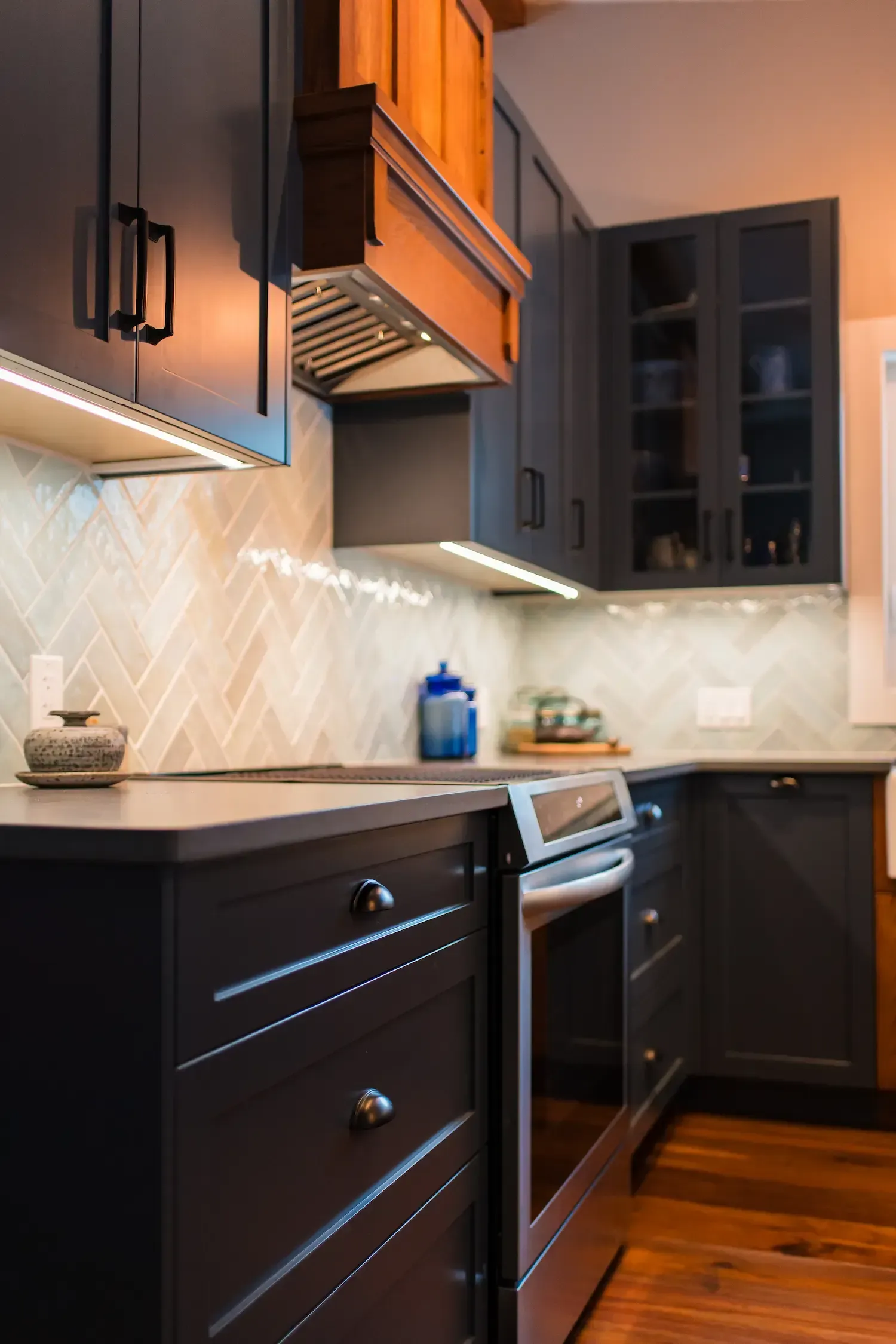 Modern kitchen with dark cabinets, stainless steel appliances, white backsplash, and warm wood floors