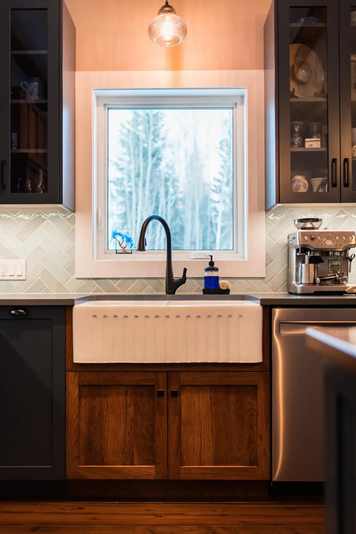 Modern kitchen sink beneath a bright window, with dark cabinets and a white farmhouse sink.