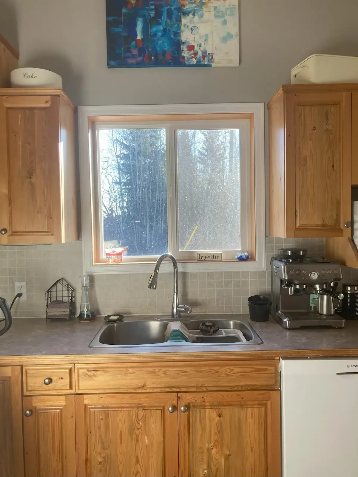 Kitchen sink beneath window with wooden cabinets and a coffee maker on the right