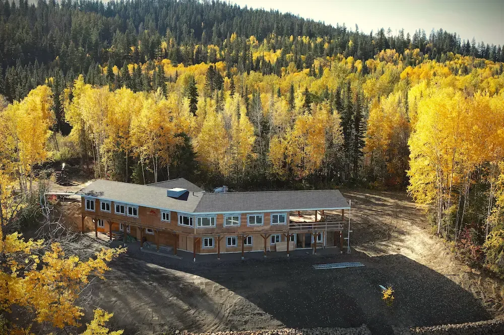 Rustic lodge surrounded by bright yellow autumn trees at the edge of a forested hillside
