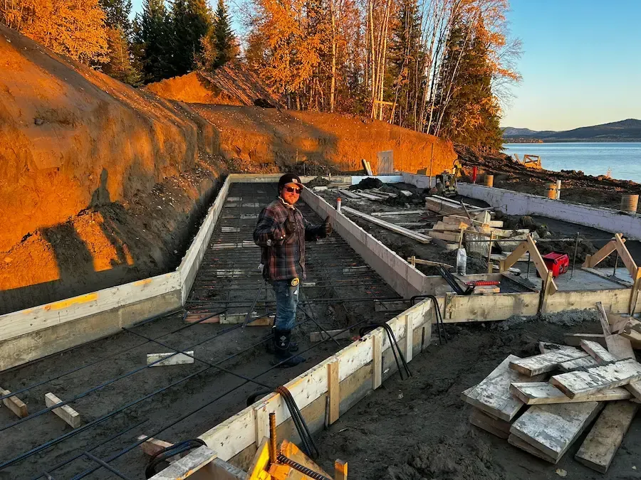 Person standing amid a damaged waterfront walkway at sunset, with broken concrete and debris beside the water.