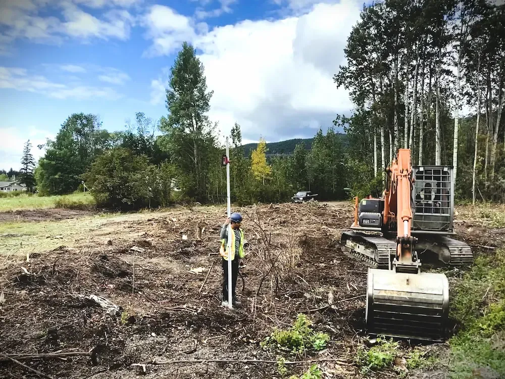 Construction worker beside excavator in a cleared field under a partly cloudy sky
