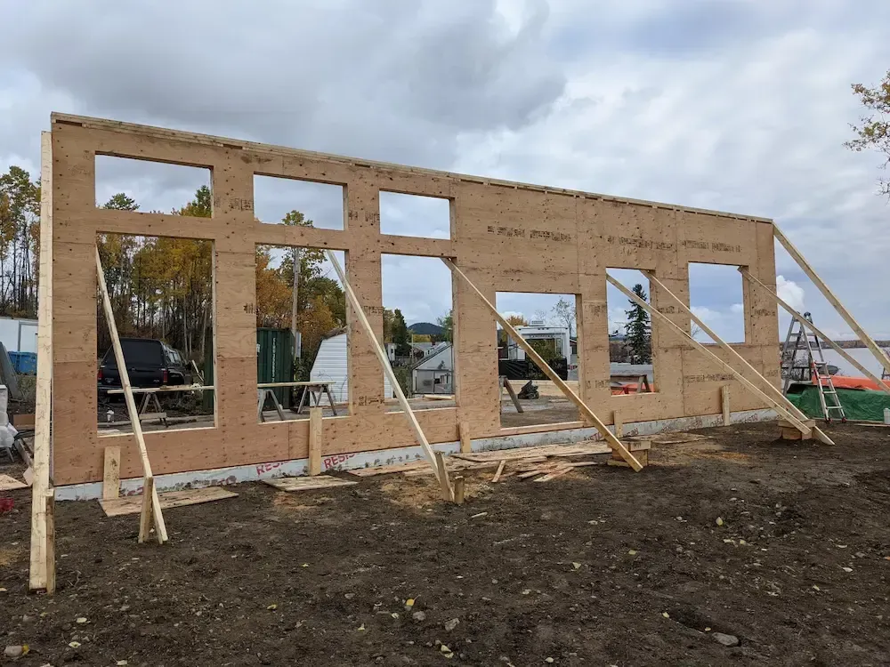 Partially framed wooden wall under construction with several window openings and support braces outdoors