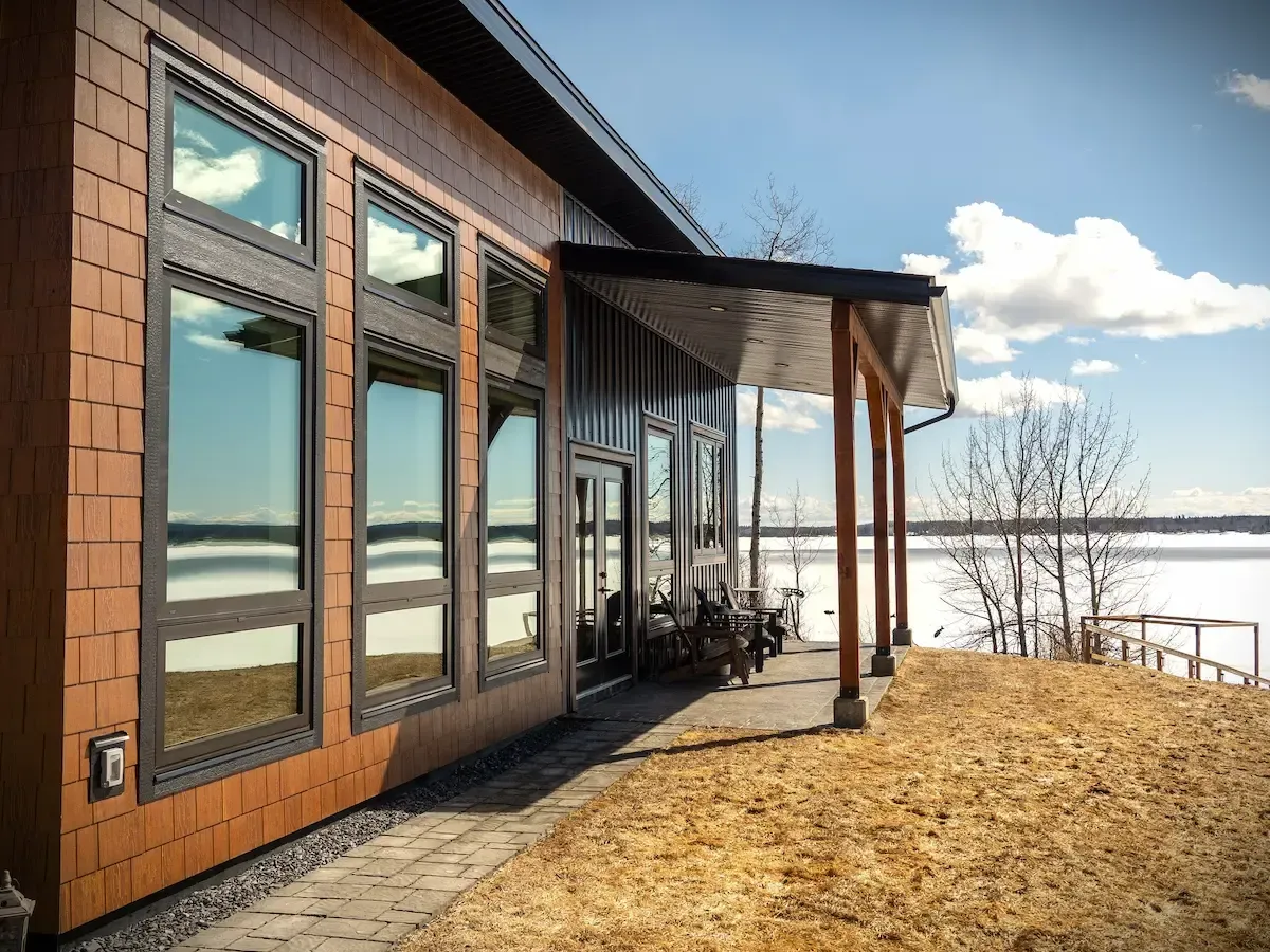 Modern cabin with large windows on a snowy lakeside, viewed from a dry brown hillside