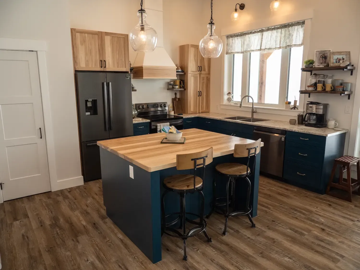 Modern kitchen with dark cabinets, wood island, stainless fridge, and large window over sink.