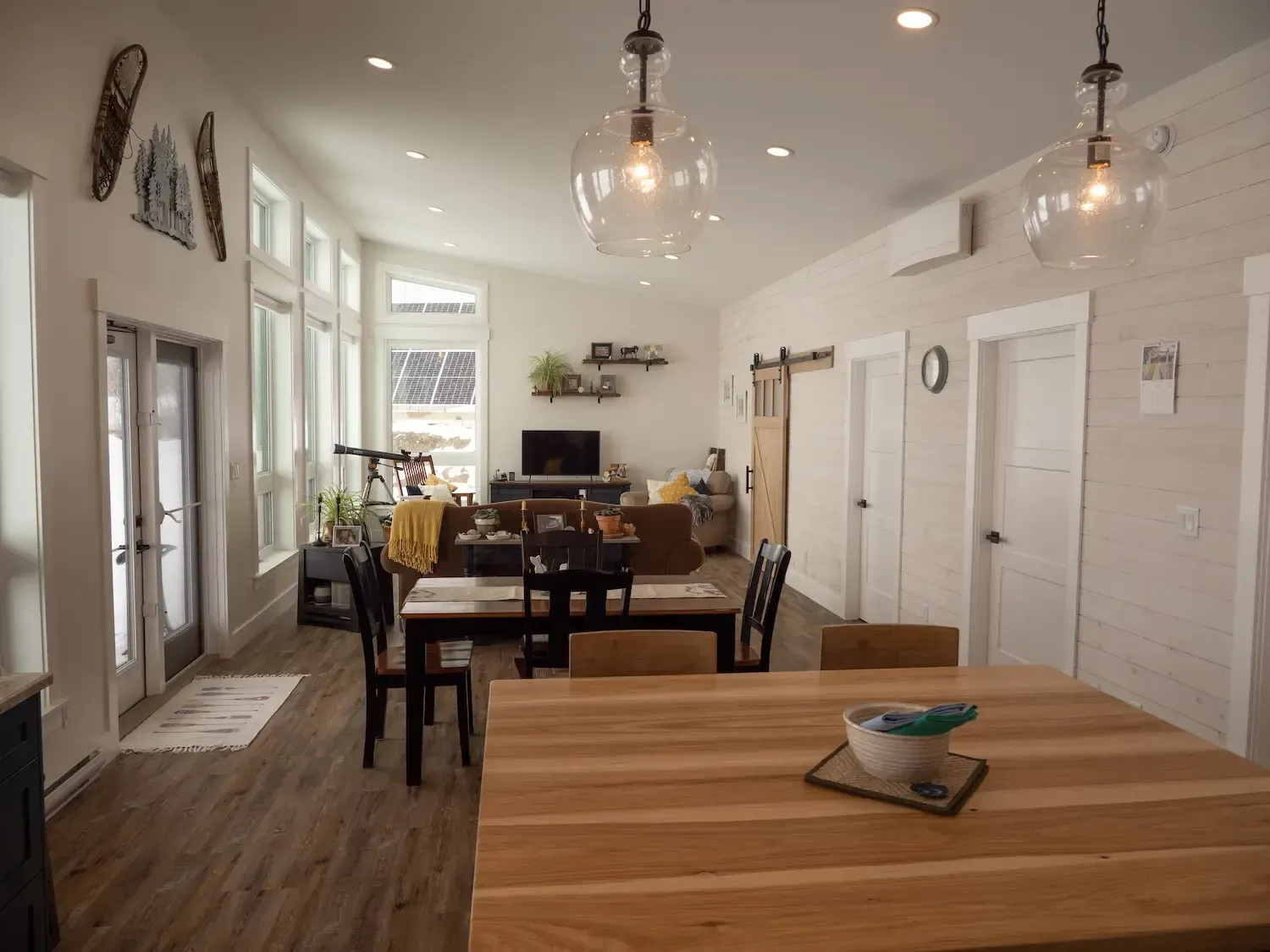Bright open dining room with long wooden table, hanging lights, and white walls
