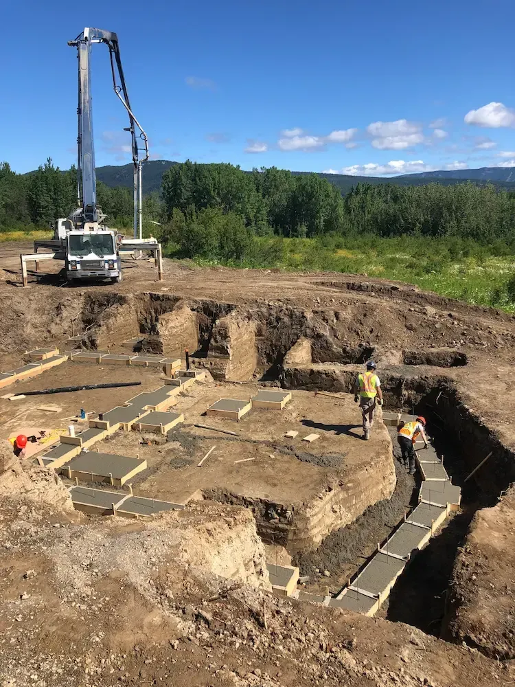 Archaeological excavation site with a digger, exposed foundations, and workers under a blue sky