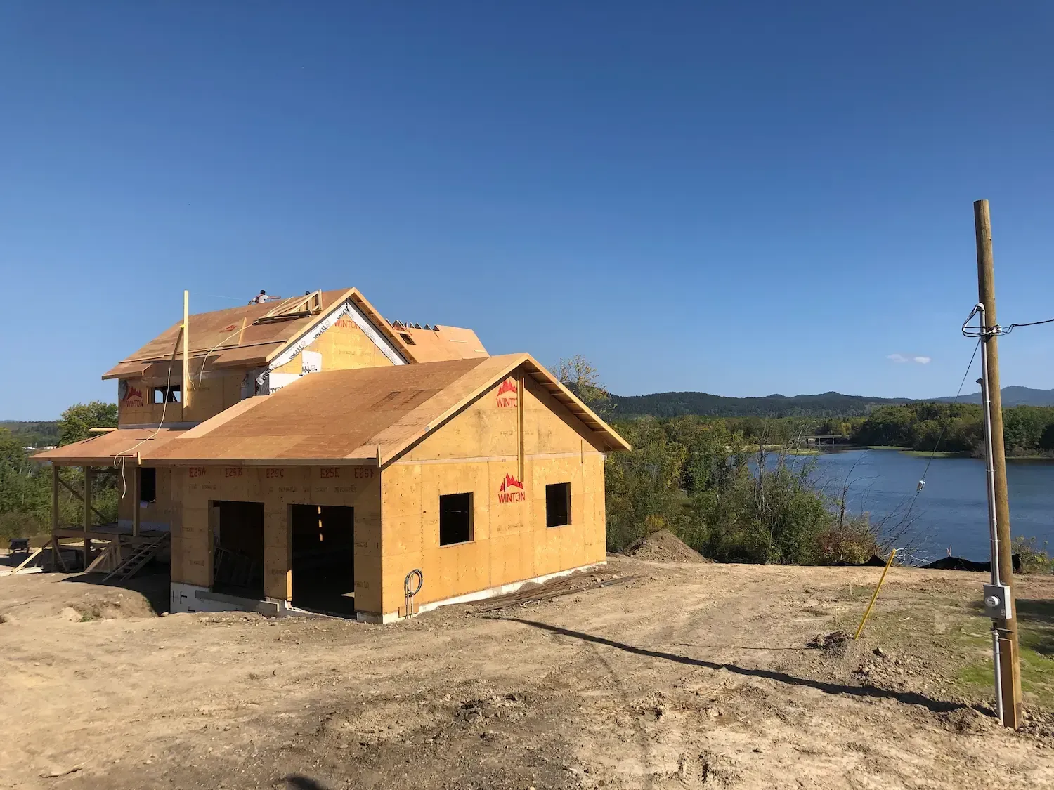 Partially built yellow house by a lake under a clear blue sky