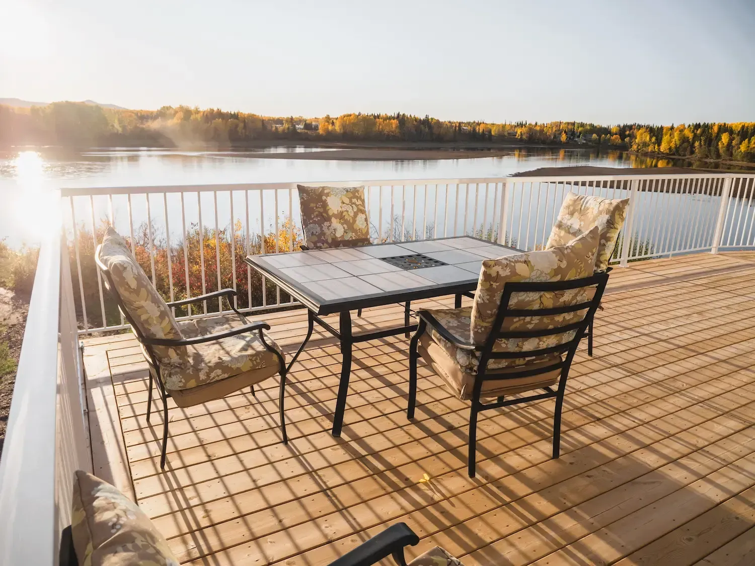 Patio table and chairs on a wooden deck overlooking a calm lake at sunset