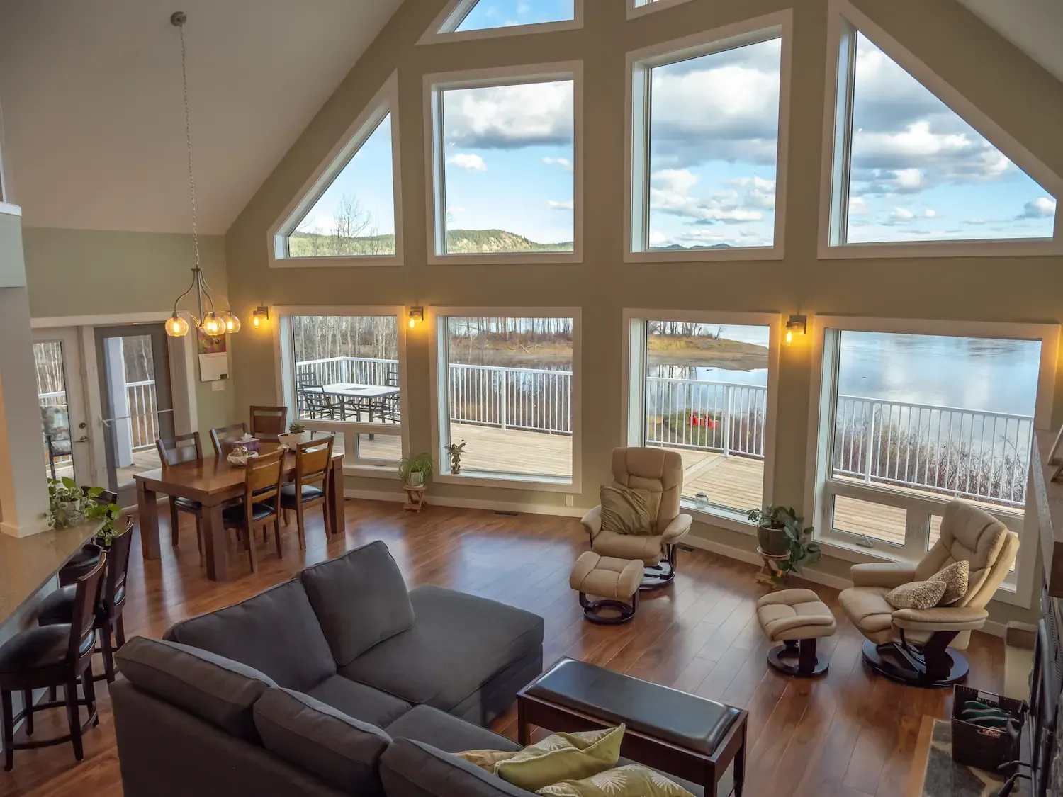 Bright living room with large windows, dark sofa, dining table, and two tan chairs overlooking a snowy view