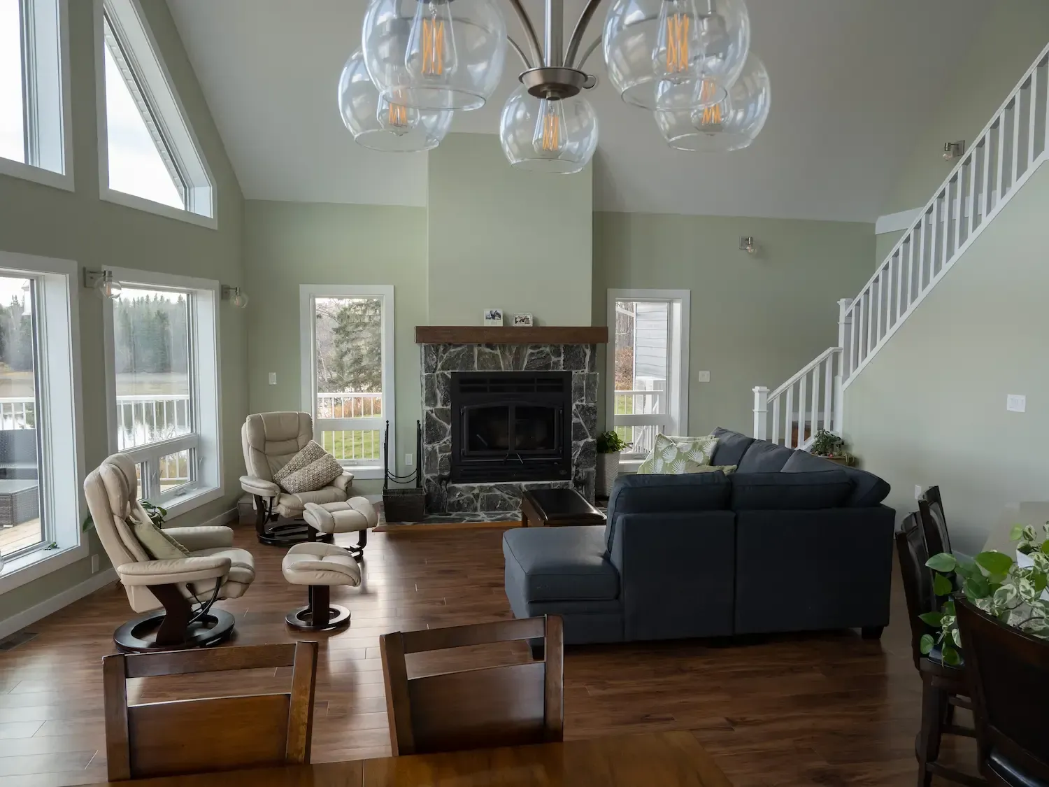 Bright living room with high windows, fireplace, dark sofa, and wood floors, viewed from the stairway.