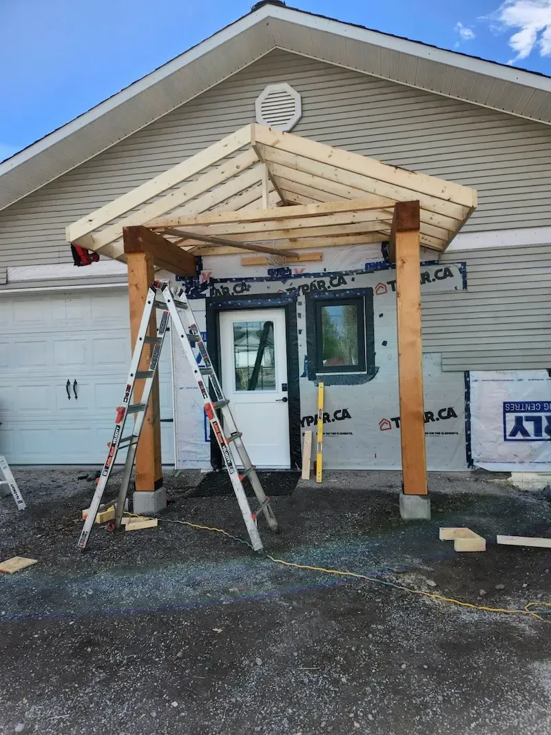 Construction work at a building entrance with scaffolding, ladders, and a newly framed awning.