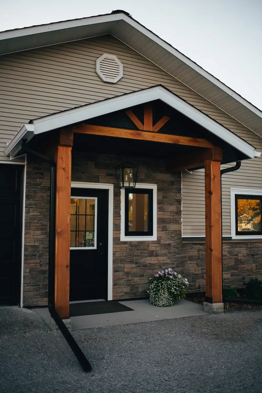 Front entrance of a brick house with a covered porch, wooden posts, and gravel walkway.