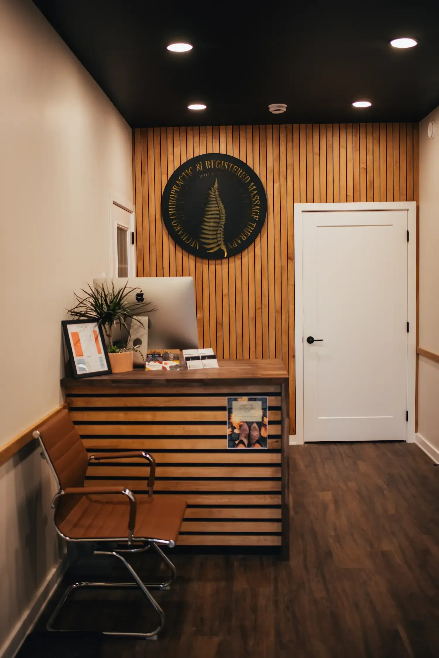 Small reception desk in a narrow hallway with wood paneling, black ceiling lights, and a white door.