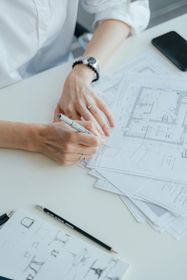 Two people reviewing architectural blueprints on a desk, one sketching with a pen