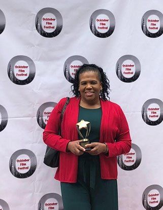 Jillian Bullock holding a gold star trophy at the October Film Festival backdrop