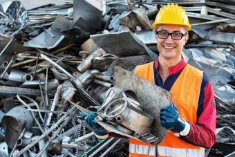 Un operaio sorridente con elmetto e giubbotto di sicurezza maneggia rottami metallici in un centro di riciclaggio.
