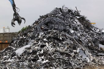 Cumulo di rottami metallici in un cortile con una gru che solleva i detriti.
