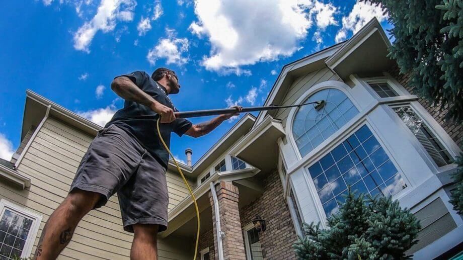 A man is cleaning the windows of a house with a high pressure washer.