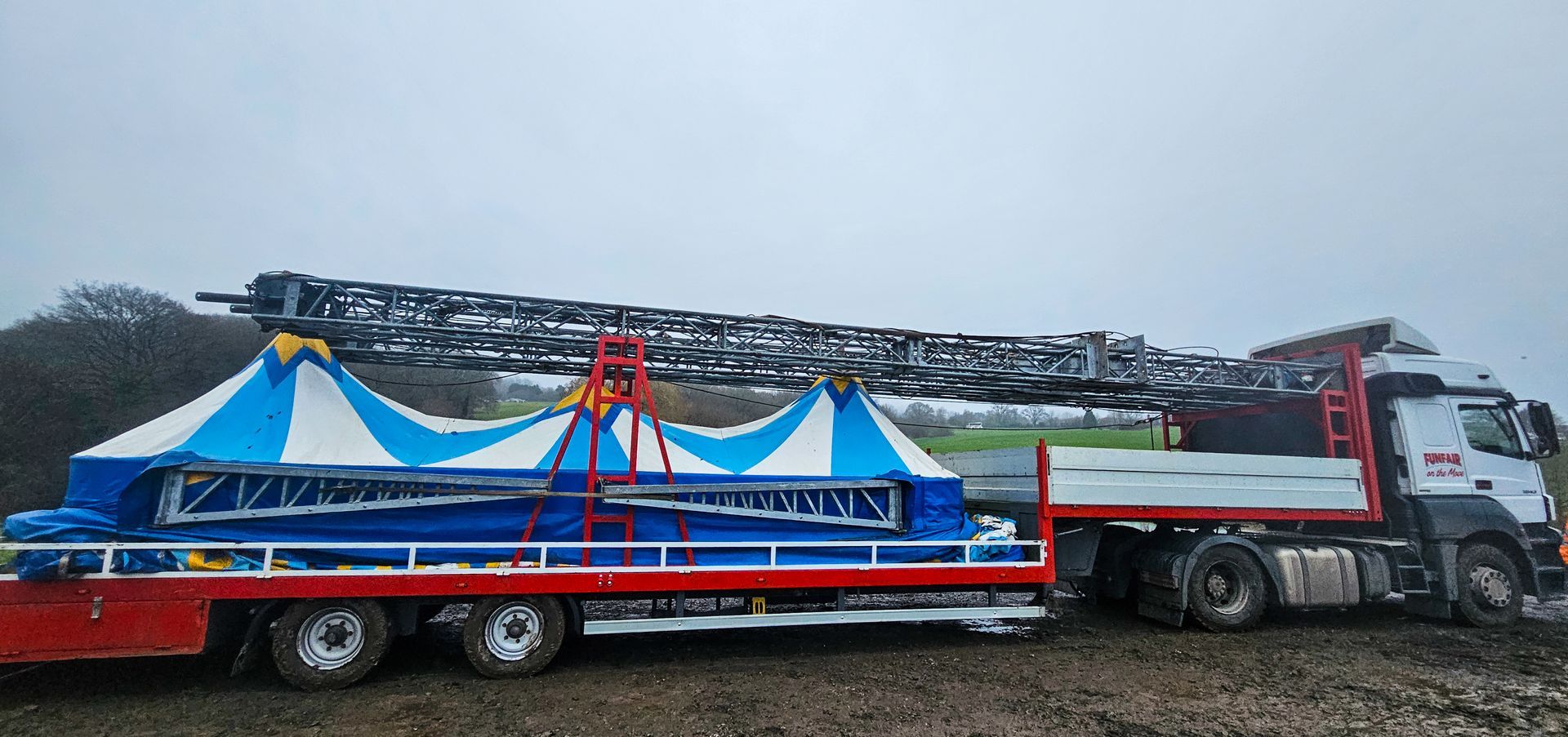 A red and white truck is carrying a blue and white circus tent