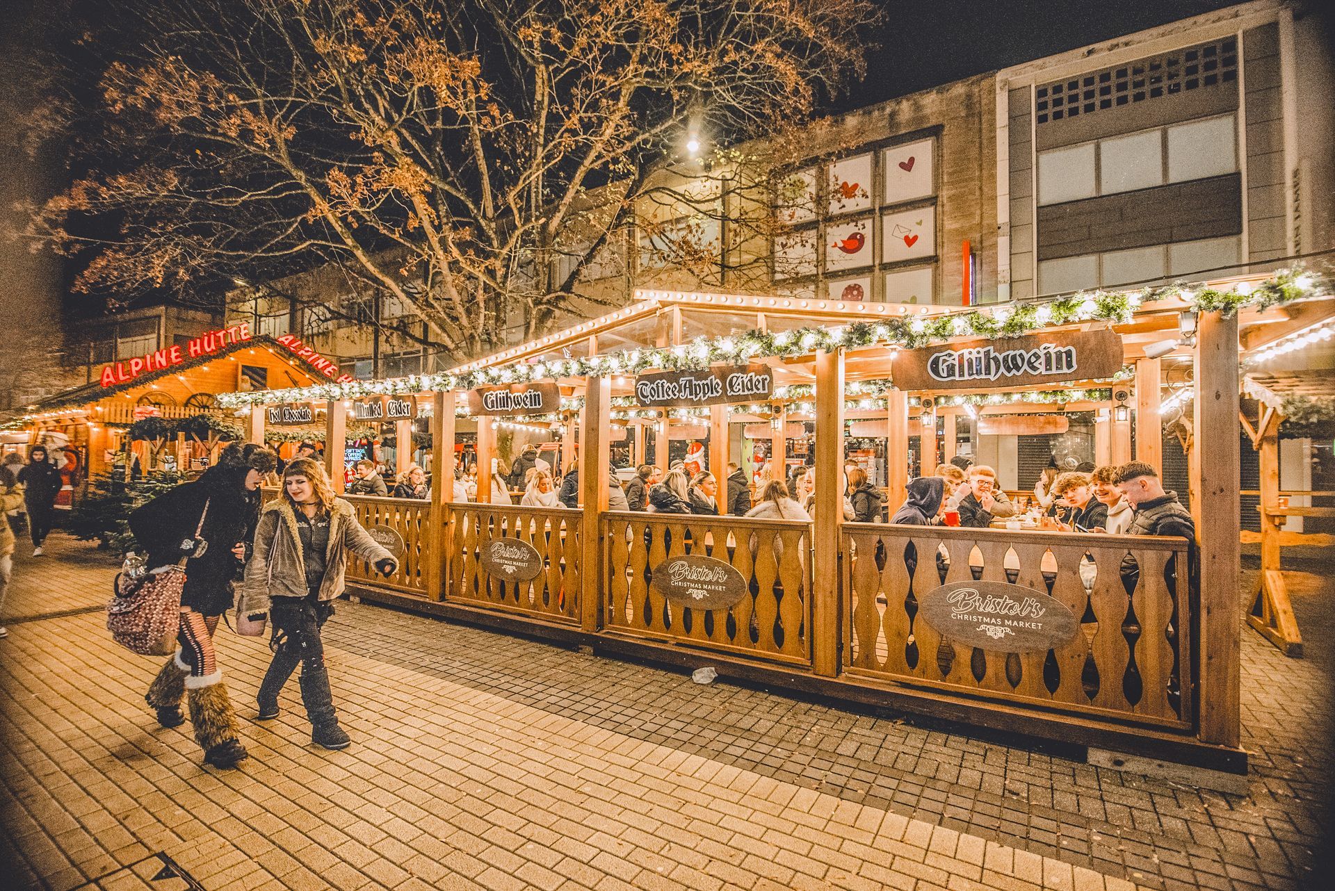 Christmas market at night with wooden stalls and people.