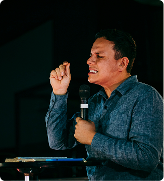 Speaker holding a microphone and gesturing while speaking on stage against a dark background