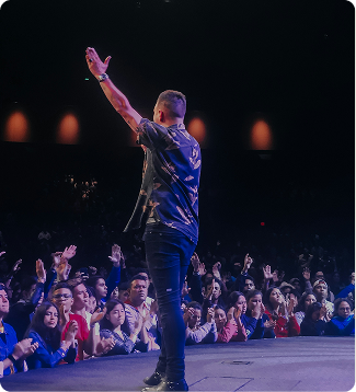 Singer on stage with raised arm, facing a cheering crowd in a dark concert venue.