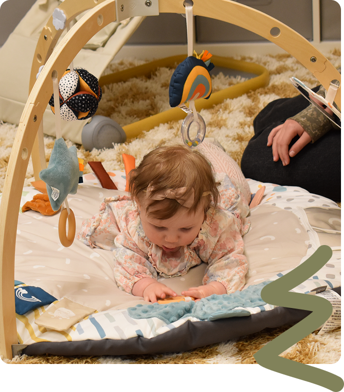 Baby playing on a white activity mat under a hanging toy arch.