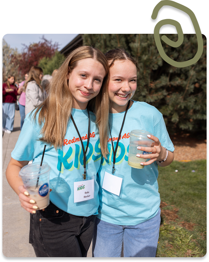Two smiling friends in matching blue shirts pose outdoors, one holding a water bottle.