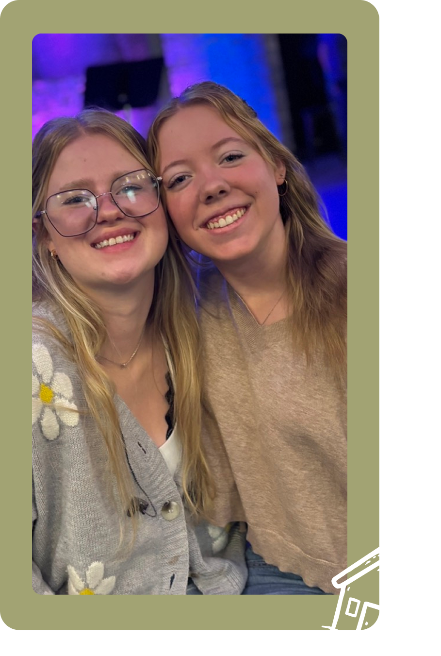 Two smiling friends posing together indoors with blue lights in the background