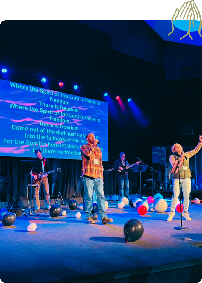Band performing on stage with blue lighting and projected lyrics, balloons scattered on the floor.