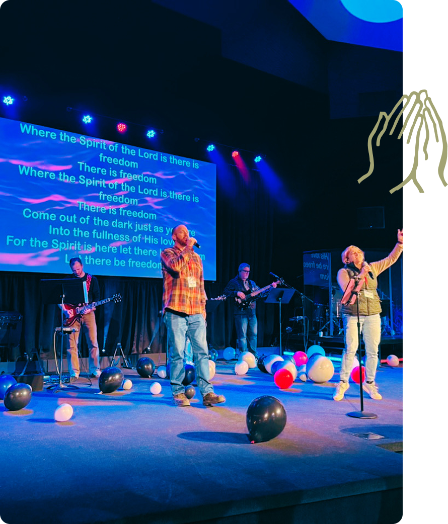Band performing on lit stage with balloons and projected lyrics in the background