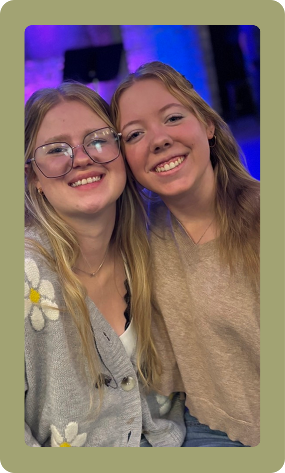 Two smiling friends posing closely indoors with purple lighting in the background