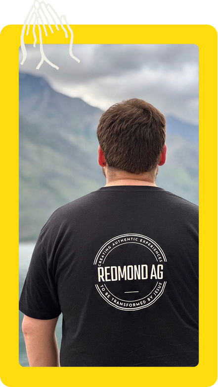 Person from behind in a black REMOND AG T-shirt, standing before a misty mountain landscape.