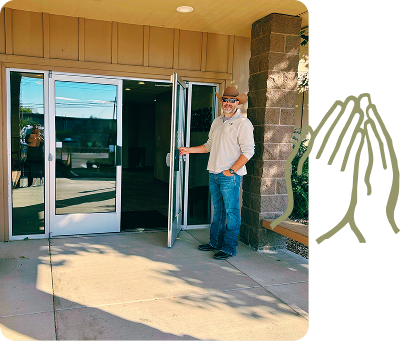 Man standing by open glass doors at a building entrance, wearing a mask and jeans.