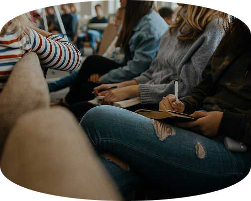 Seated people in a lecture hall, one taking notes on a clipboard