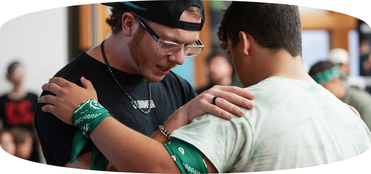 Two people in green wristbands embrace in a crowded indoor setting