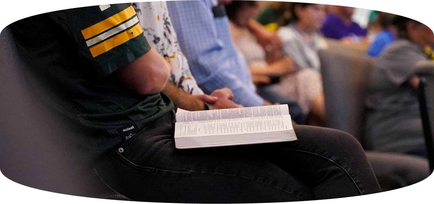 Person in a dark shirt holding an open notebook while seated in a classroom or lecture hall