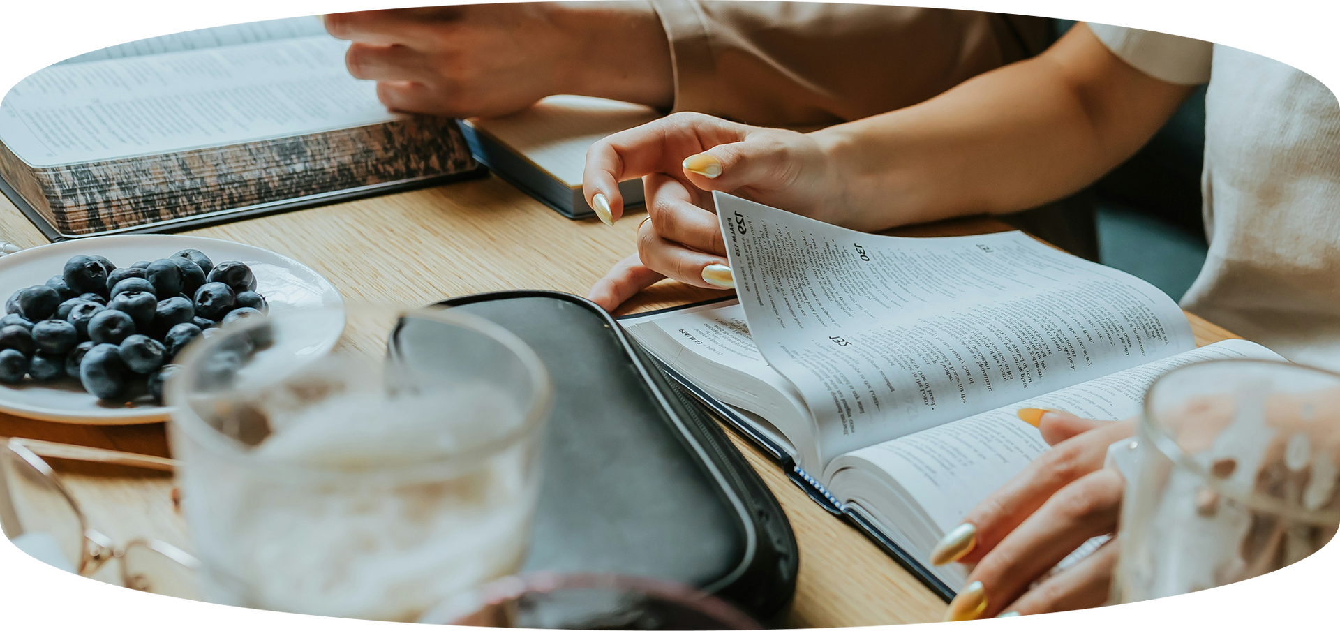 People studying at a table with an open book, notebook, coffee, and blueberries
