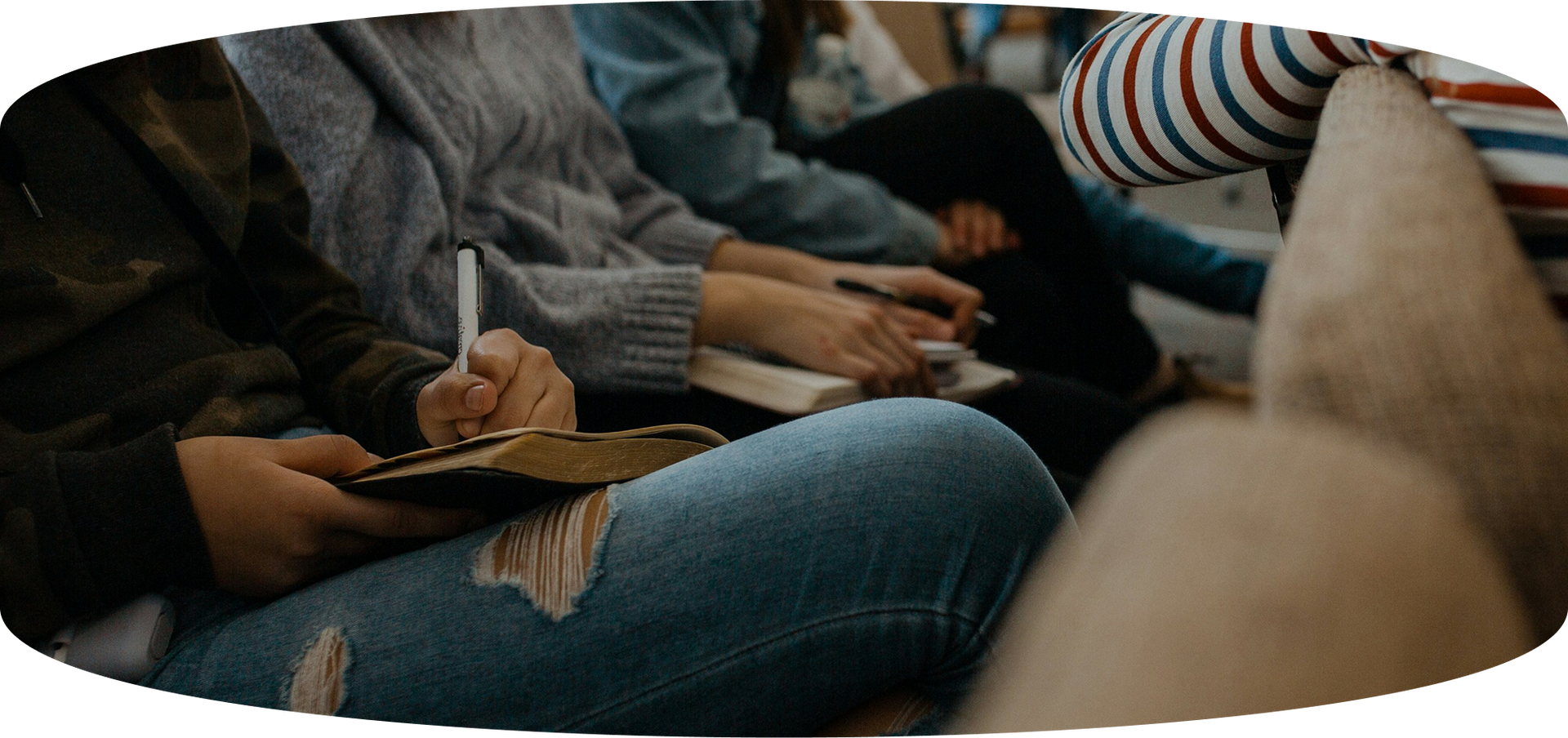 People seated close together, writing in notebooks during a meeting or class.