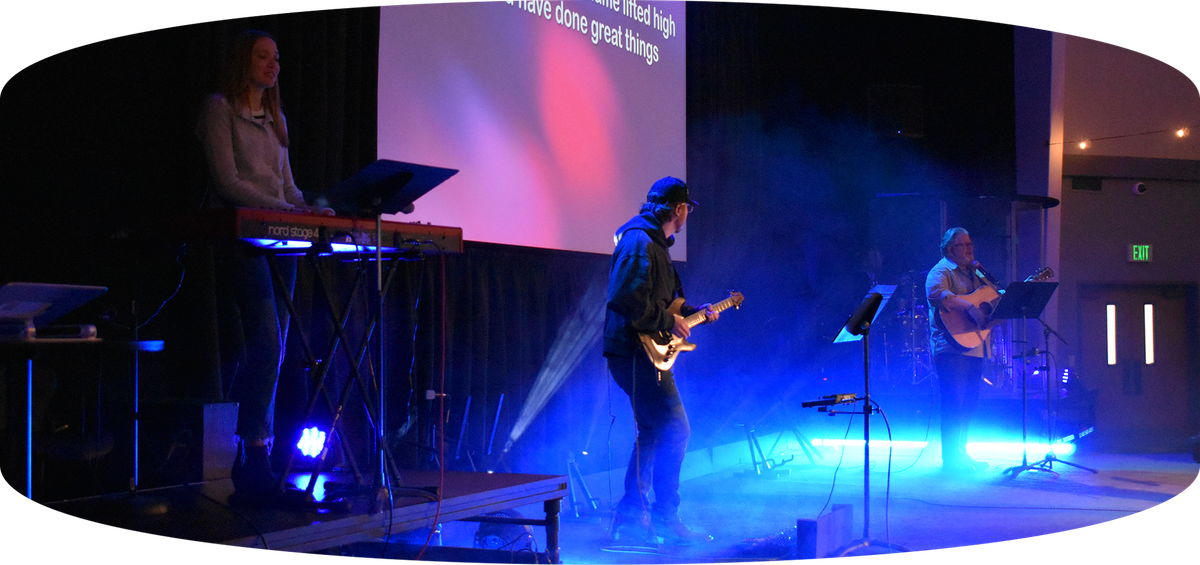 Blue-lit live band performing on stage with keyboards, guitar, and microphones
