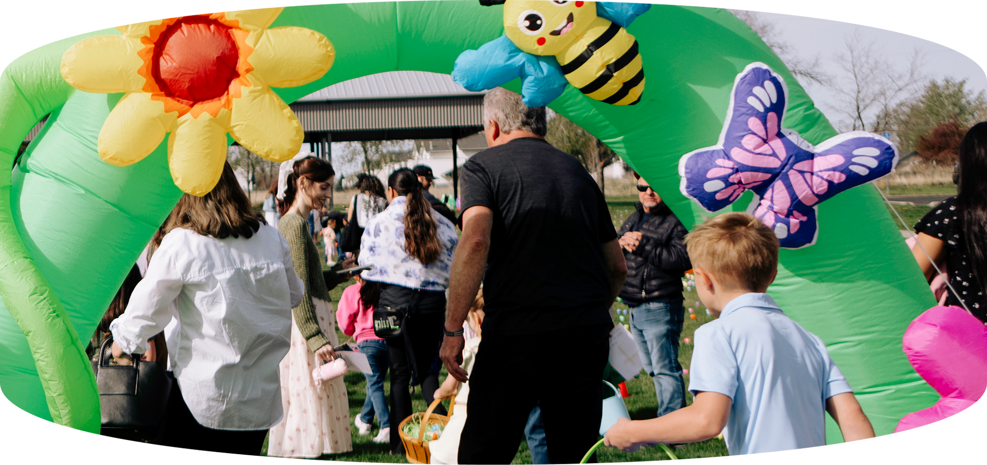 People walking through a colorful inflatable arch at an outdoor event, with flower and butterfly decorations