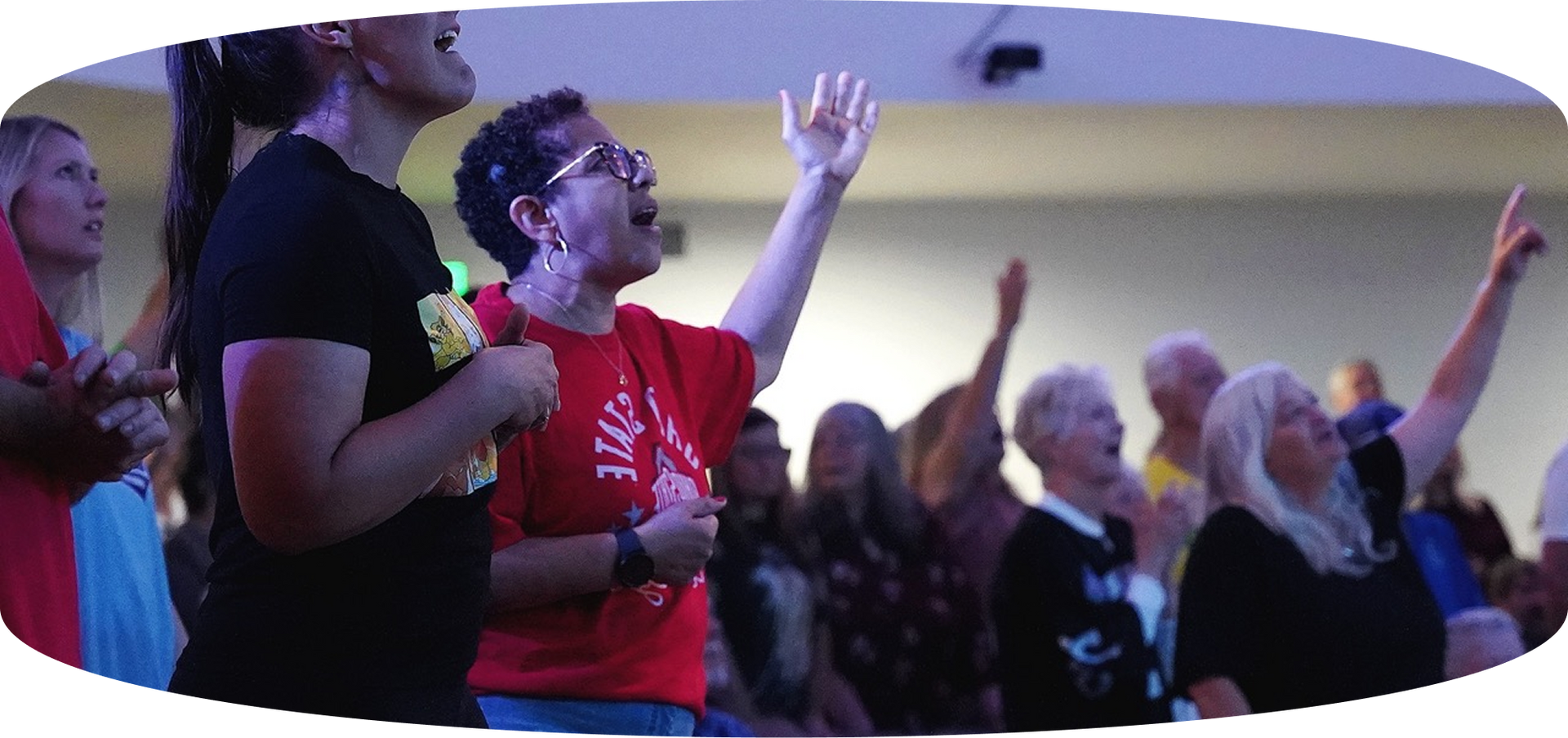 People worshipping with raised hands in a crowded indoor church service