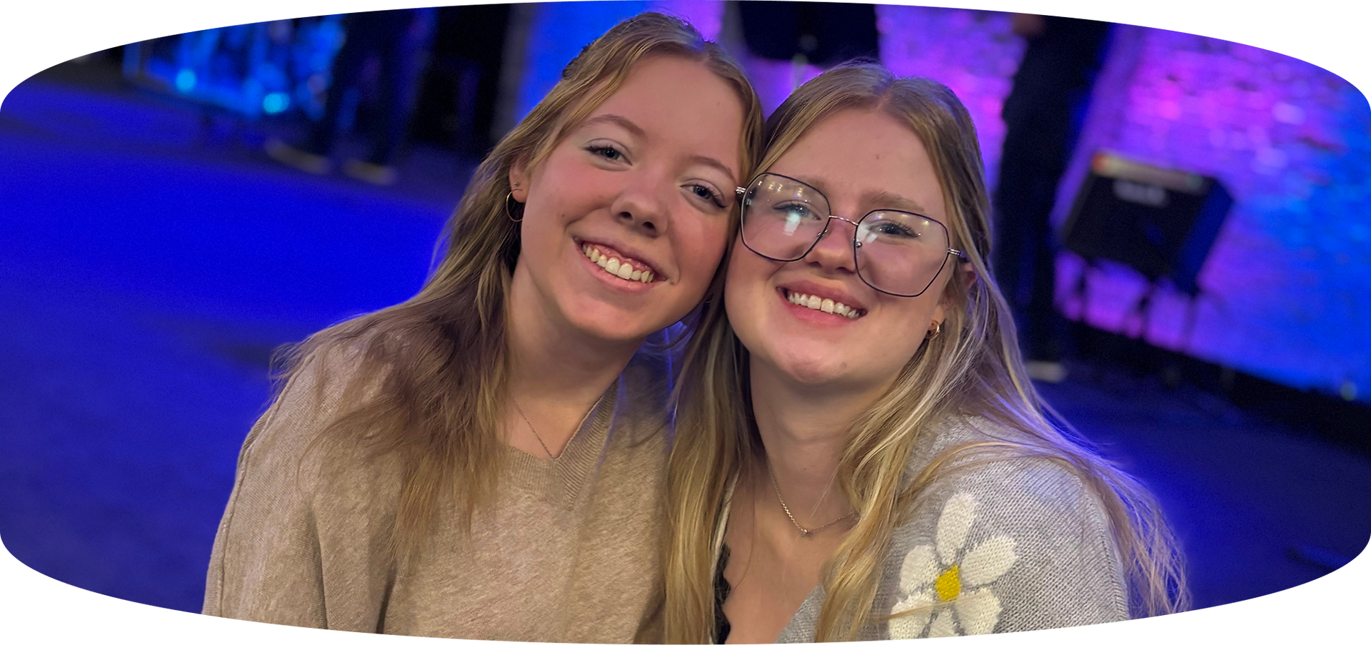 Two smiling friends posing together in blue-purple event lighting