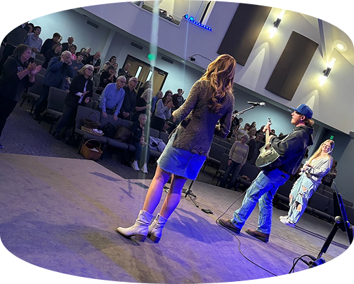 Musicians performing onstage in a church auditorium, with an audience seated nearby.