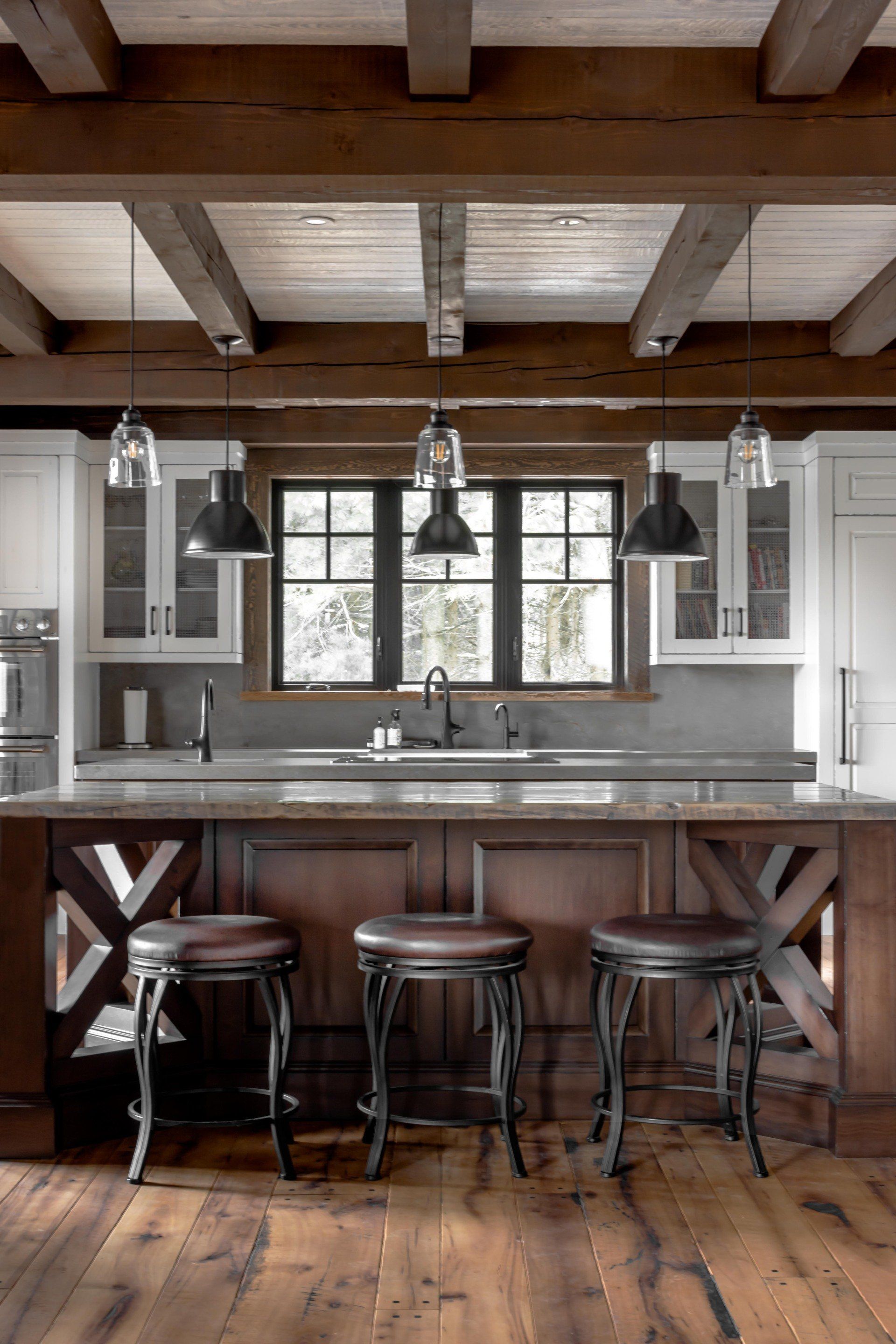 Rustic kitchen with wooden beams, dark cabinets, island with stools, and window with outdoor view.