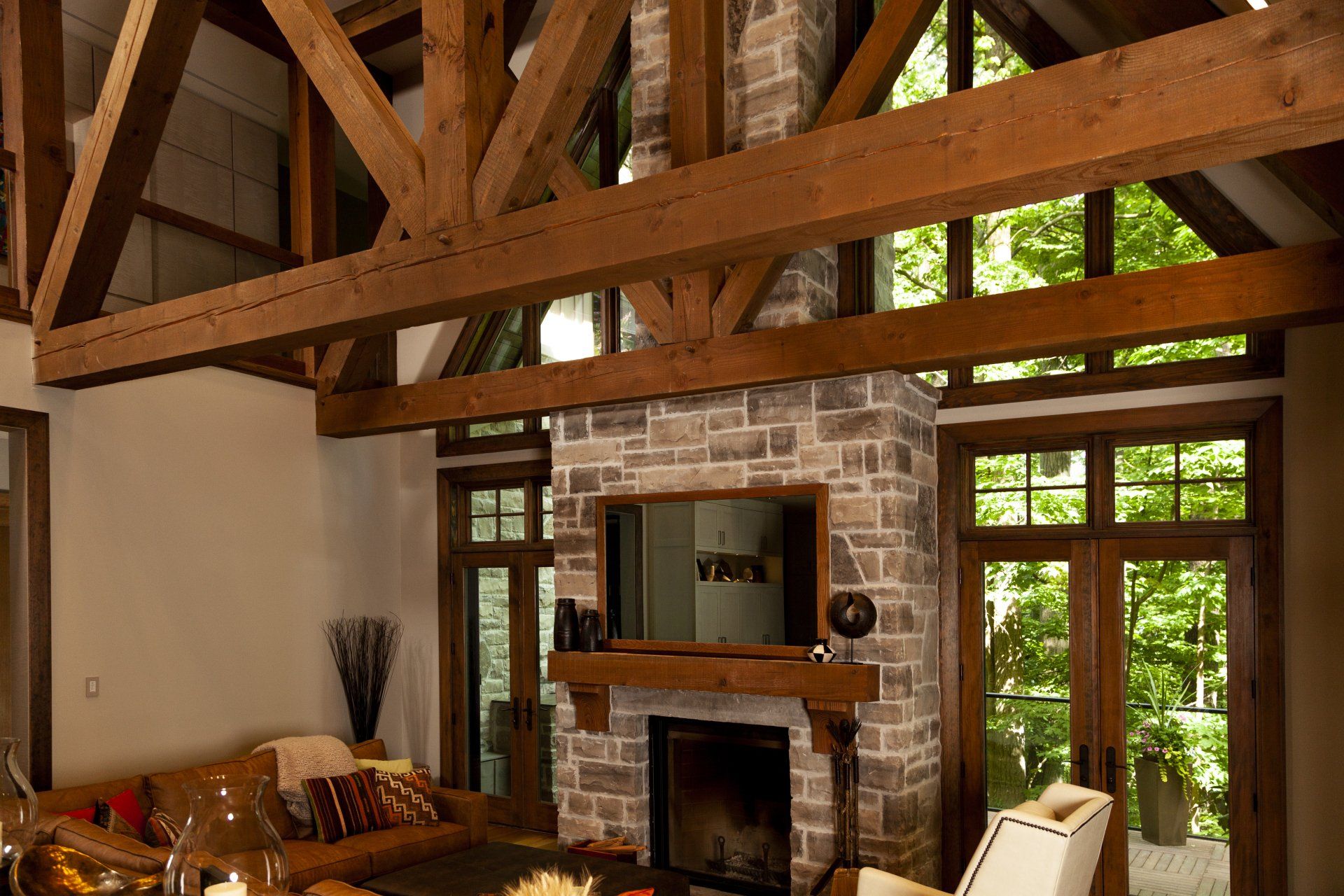 Living room with stone fireplace, wooden beams, windows, and leather sofa.