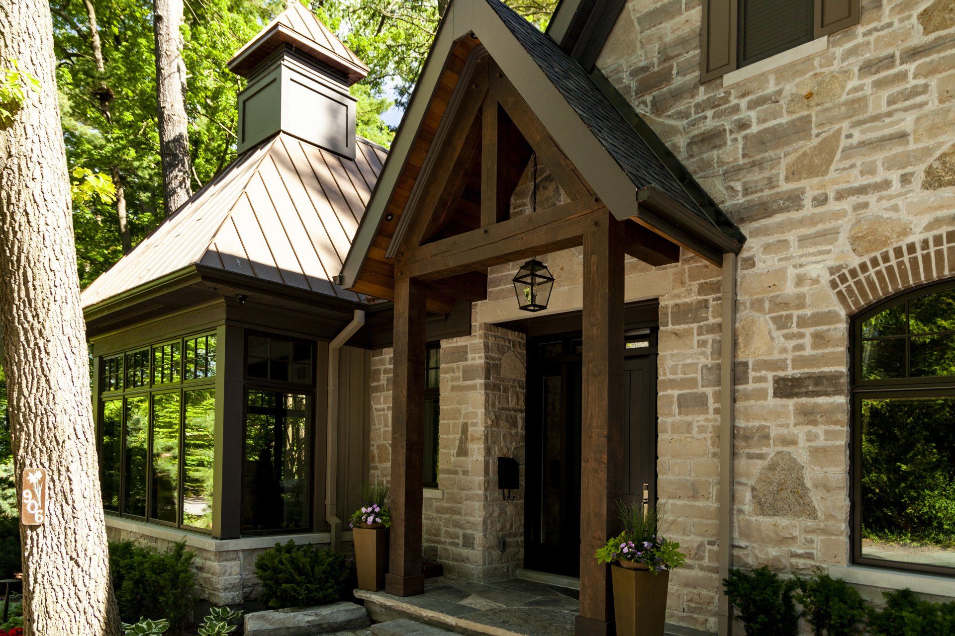 A large stone house with a wooden timber frame porch and a roof