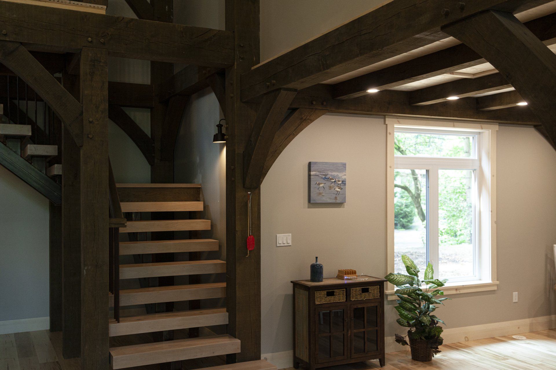 Interior with wooden beams, staircase, and a window overlooking a green outdoor view.